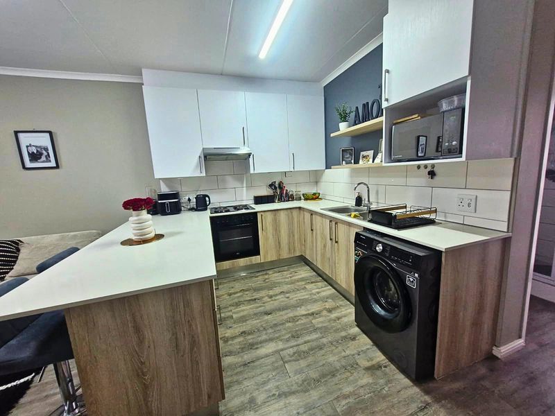 Modern open-plan kitchen featuring light wood-grain cabinetry, white countertops, integrated appliances, and a breakfast bar, creating a functional and contemporary cooking space.