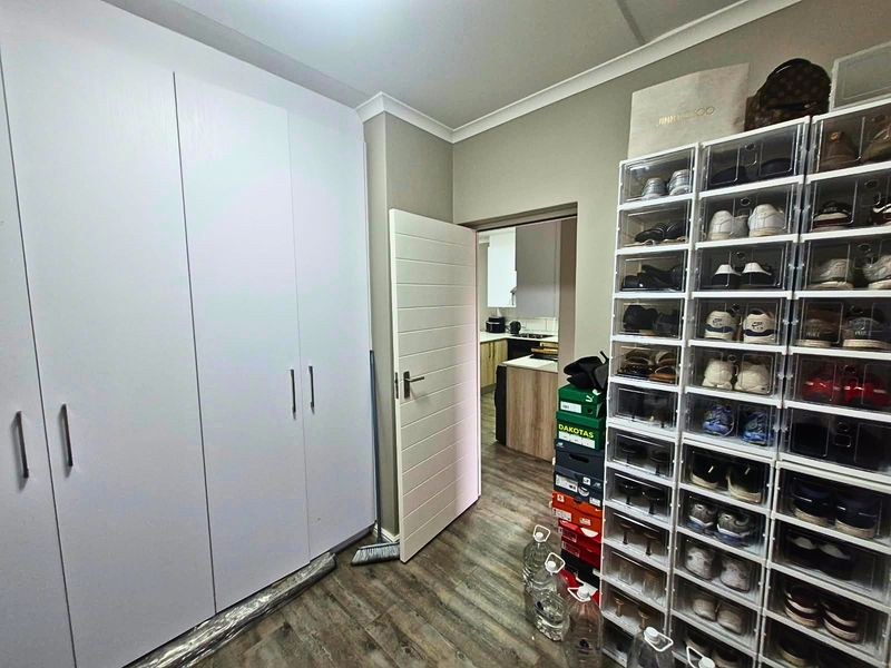 Bedroom featuring built-in cupboards, laminate flooring, and neutral wall finishes, with a view through to the adjacent kitchen area.