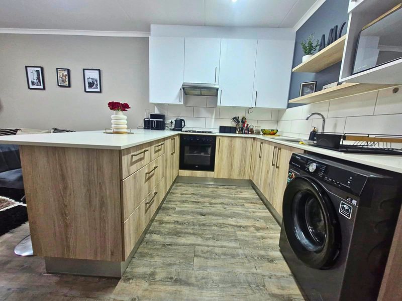 Modern kitchen featuring light wood-look cabinetry, white countertops, built-in oven, extractor fan, and integrated laundry plumbing, offering a functional and contemporary workspace.