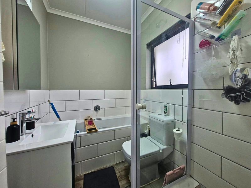 A functional bathroom featuring a built-in vanity, bathtub, toilet, and a glass-enclosed shower area with modern white subway-style wall tiling.