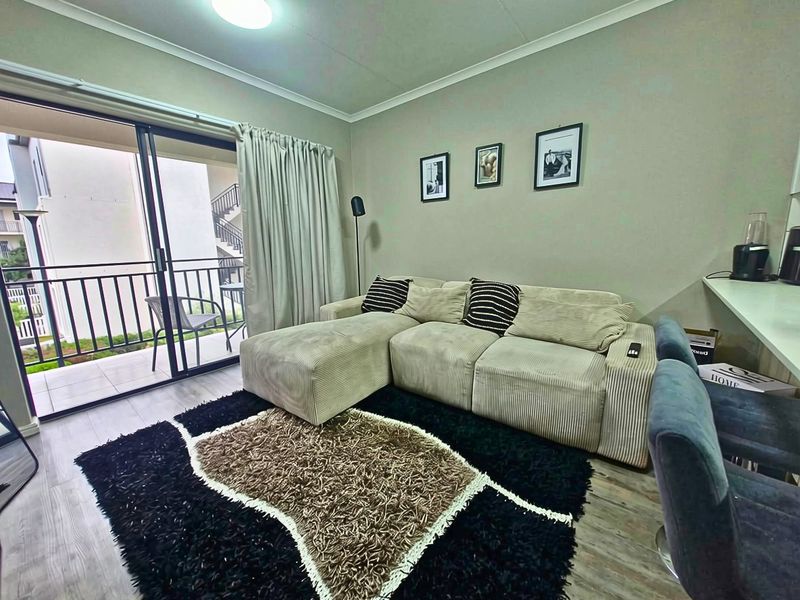 A well-maintained living room featuring laminate flooring and a large sliding glass door providing direct access to a private balcony.