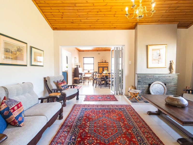Open-plan living area featuring a timber-clad ceiling, brick fireplace, and folding glass doors leading to an adjacent dining space.