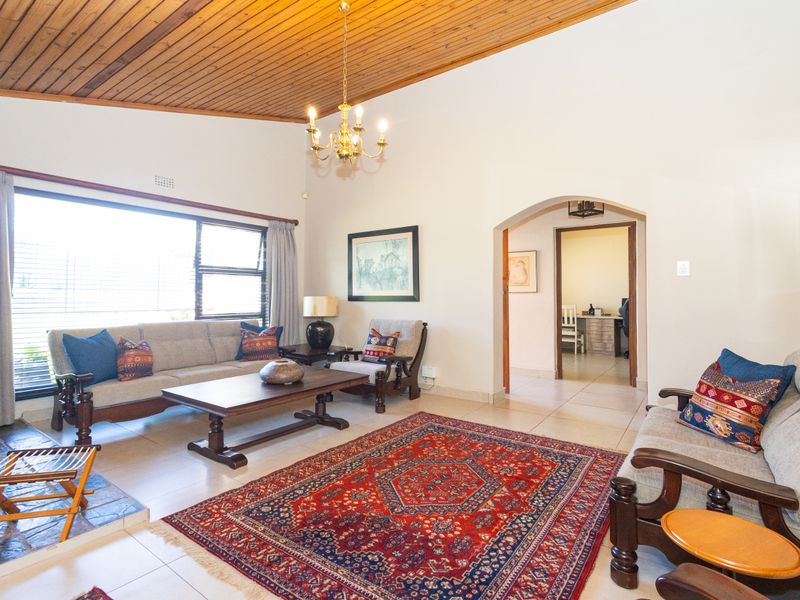 Spacious living room featuring a vaulted timber ceiling, tiled flooring, and a stone fireplace hearth, with an arched entryway leading to an adjacent room.