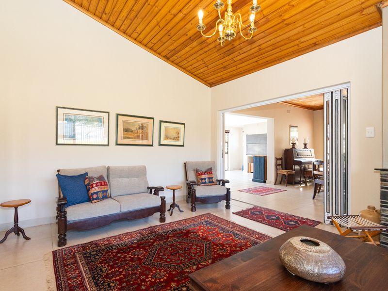 Spacious living room featuring a vaulted timber ceiling, tiled flooring, and a stone-clad fireplace, with folding doors leading to an adjacent dining area.
