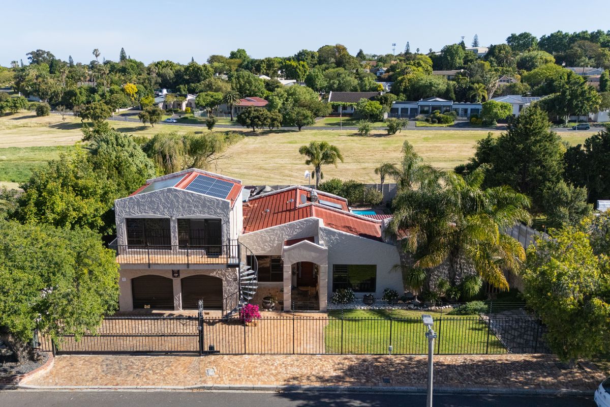 Aerial view of a residential property featuring a metal roof, solar panels, a balcony, and a double garage, set in a landscaped neighborhood.