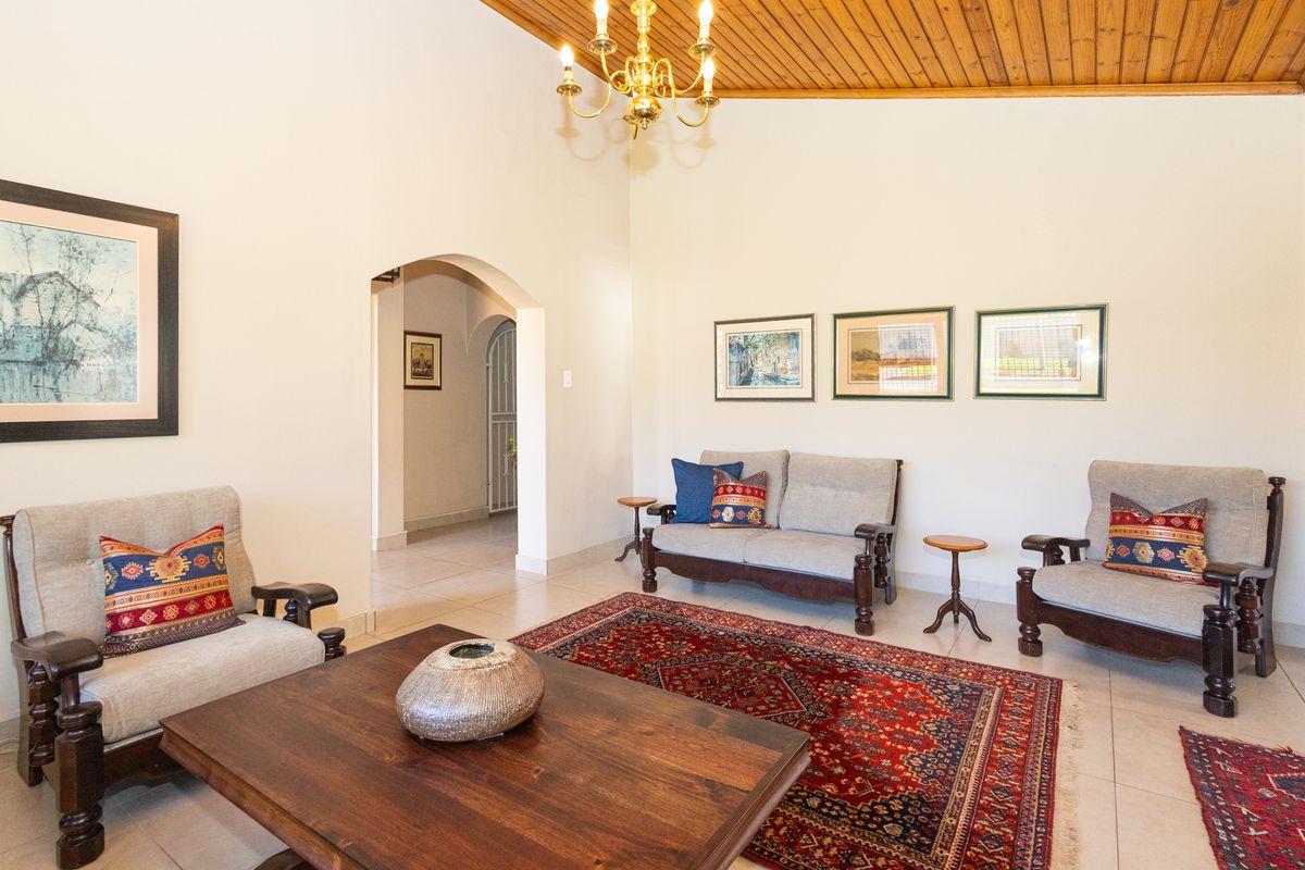 Spacious living room featuring a high vaulted timber ceiling, neutral tiled flooring, and an elegant arched doorway leading to the hallway.