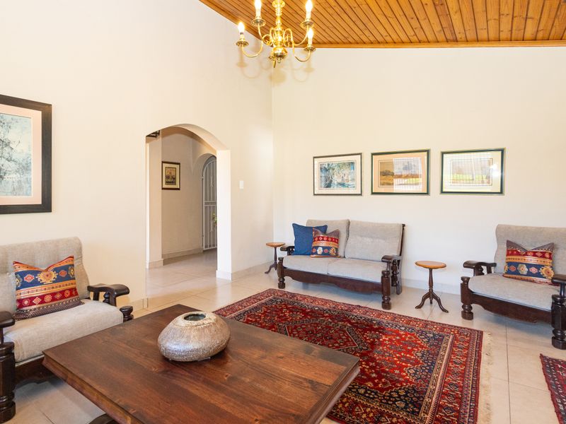 Spacious living room featuring a high vaulted timber ceiling, neutral tiled flooring, and an elegant arched doorway leading to the hallway.