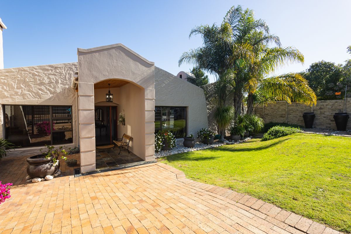 A well-maintained rear exterior featuring a brick-paved patio, covered entrance, and a landscaped garden with mature palm trees and perimeter walling.