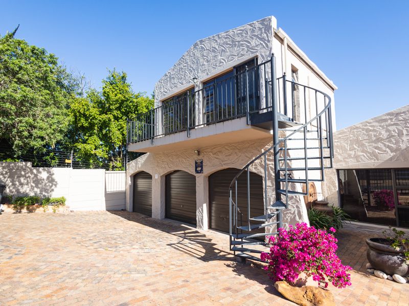 A well-maintained exterior view featuring a triple garage, a distinctive spiral staircase leading to an upper balcony, and a paved driveway area.