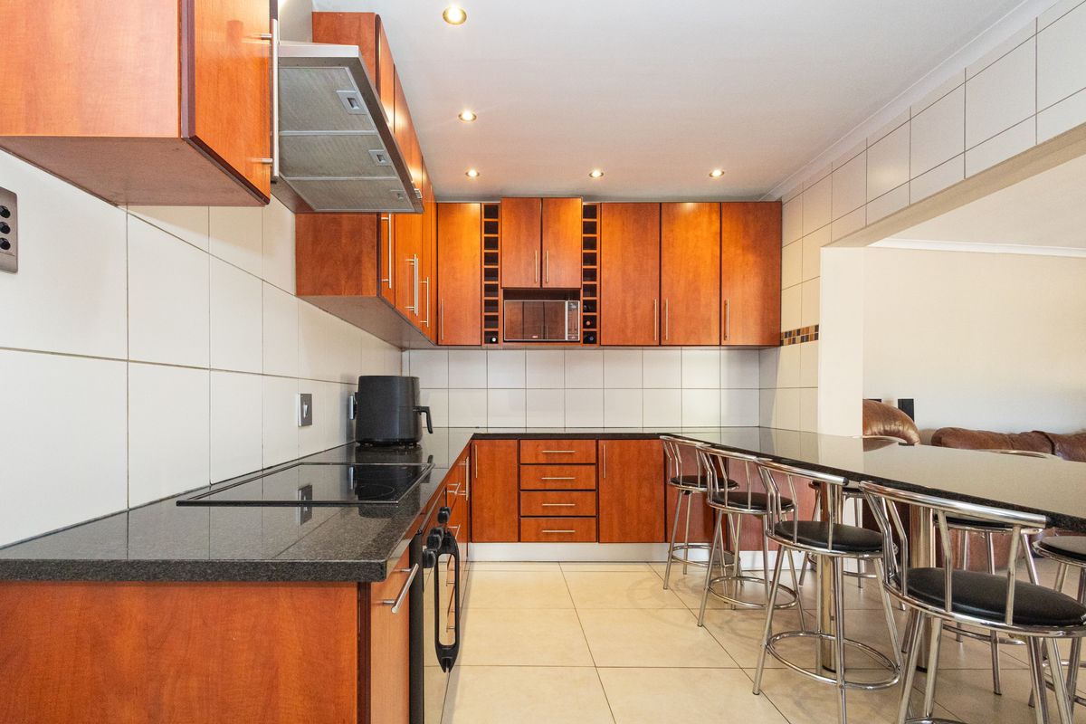 A functional kitchen featuring warm-toned wooden cabinetry, dark granite countertops, a built-in hob and oven, and a breakfast bar area.