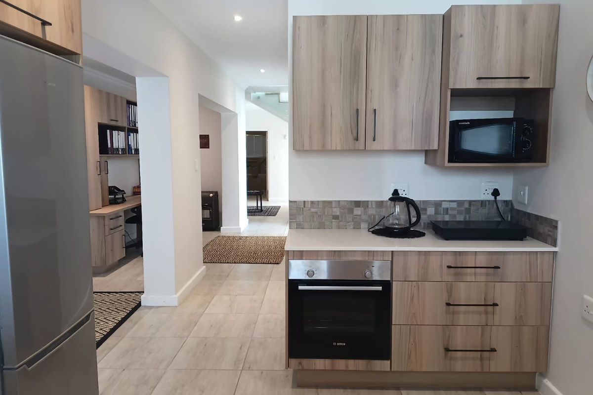 Modern kitchen area featuring light wood-grain cabinetry, stone countertops, mosaic backsplash, and integrated appliances, seamlessly flowing into an adjacent office workspace.