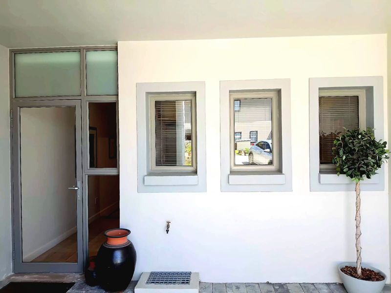Modern office entrance featuring a sleek aluminium framed glass door and matching windows with clean white exterior finishes and paved flooring.