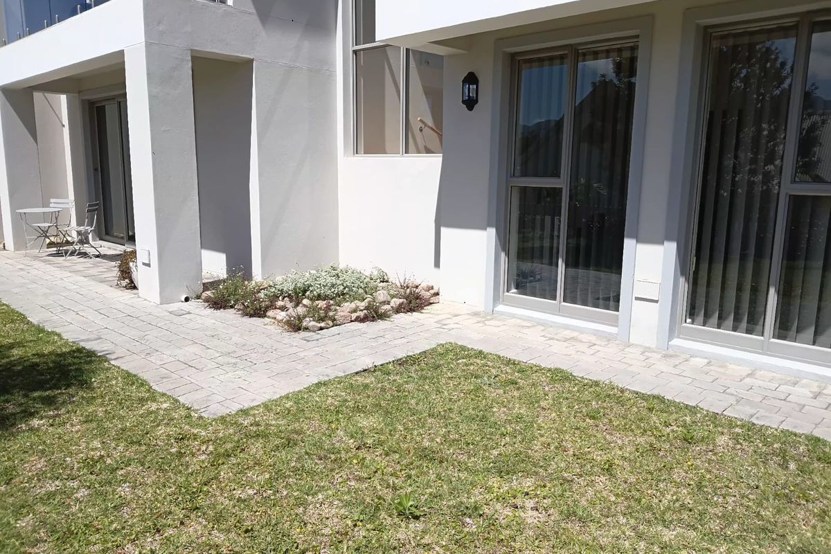 A well-maintained rear exterior view featuring a paved patio area, landscaped garden bed, and modern sliding glass doors leading into the office space.