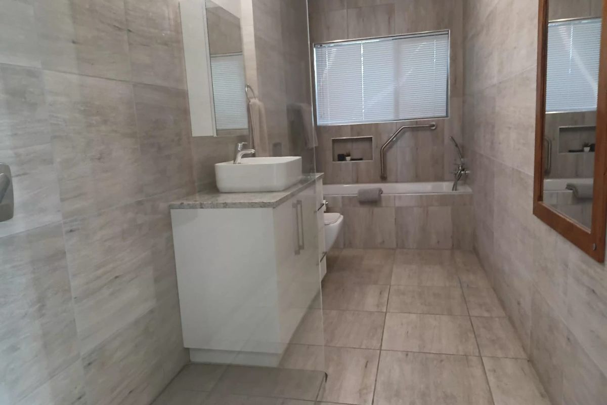Modern bathroom featuring floor-to-ceiling neutral tiling, a sleek vanity with vessel sink, a bathtub with integrated grab rail, and a glass shower screen.