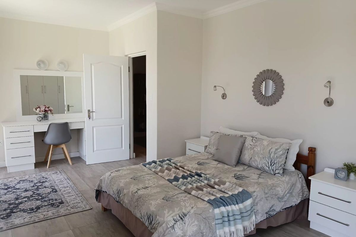 A well-maintained bedroom featuring neutral walls, laminate flooring, cove cornicing, and a built-in vanity unit with integrated mirror.