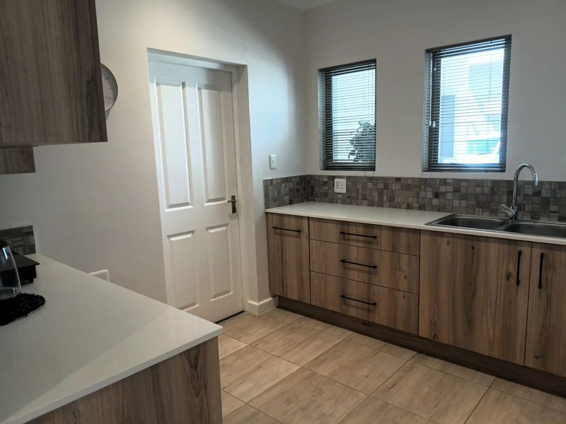 A modern, well-maintained kitchen featuring wood-finish cabinetry, stone countertops, a mosaic tile backsplash, and neutral ceramic floor tiles.