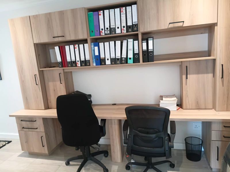 A well-organized office space featuring extensive built-in light wood cabinetry and a spacious integrated desk, providing ample storage and workspace.