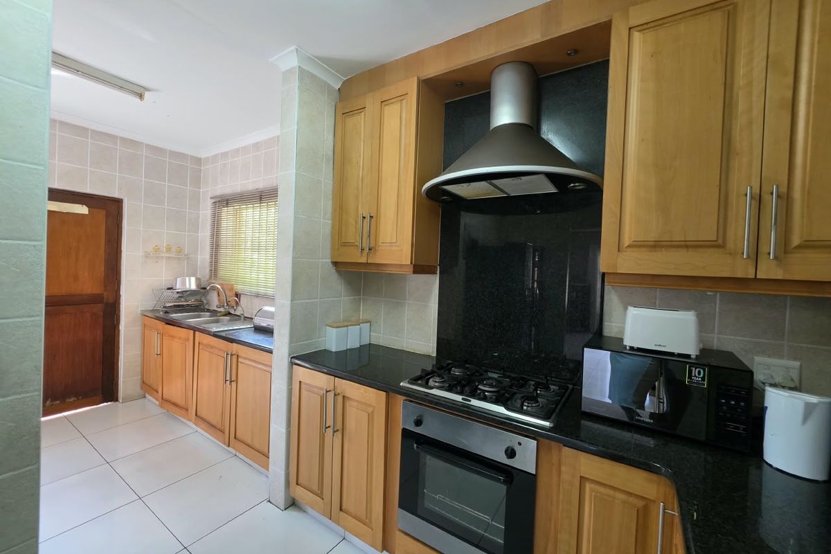 A functional kitchen featuring wooden cabinetry, granite countertops, a gas hob with extractor fan, and tiled finishes throughout.
