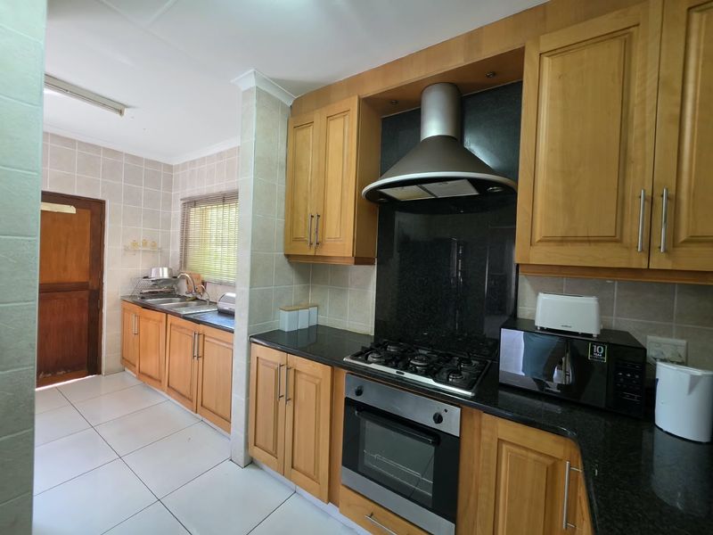 A functional kitchen featuring wooden cabinetry, granite countertops, a gas hob with extractor fan, and tiled finishes throughout.