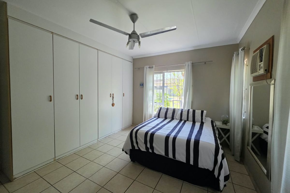A bedroom featuring tiled flooring, built-in cupboards, a ceiling fan, and a wall-mounted air conditioning unit.