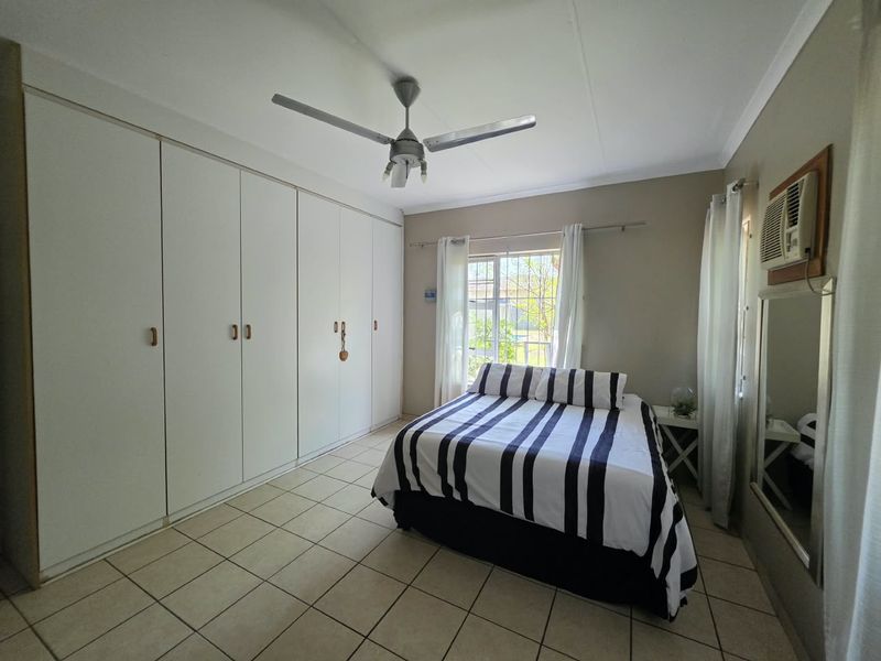 A bedroom featuring tiled flooring, built-in cupboards, a ceiling fan, and a wall-mounted air conditioning unit.
