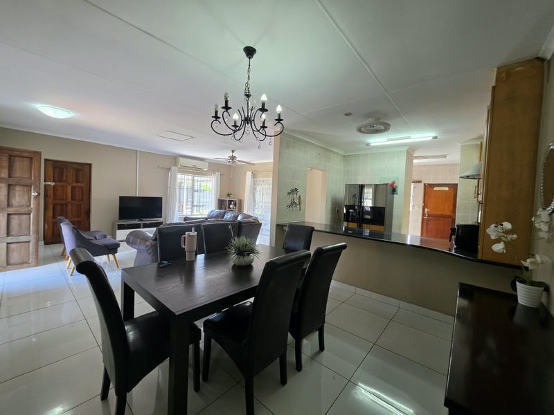 Spacious open-plan living, dining, and kitchen area featuring tiled floors, a breakfast bar, and a central chandelier, offering a functional and connected layout.
