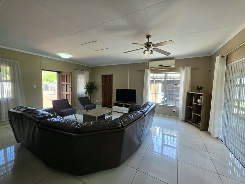 Spacious living room featuring large format floor tiles, a ceiling fan, and a wall-mounted air conditioning unit with direct access to the exterior.