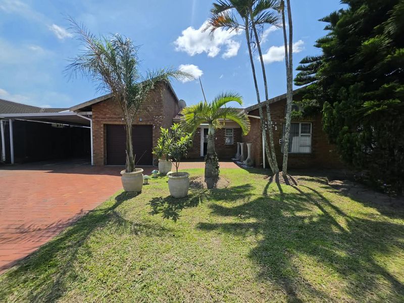 Front view of a brick house featuring a paved driveway, attached garage, and a covered carport area with established garden landscaping.