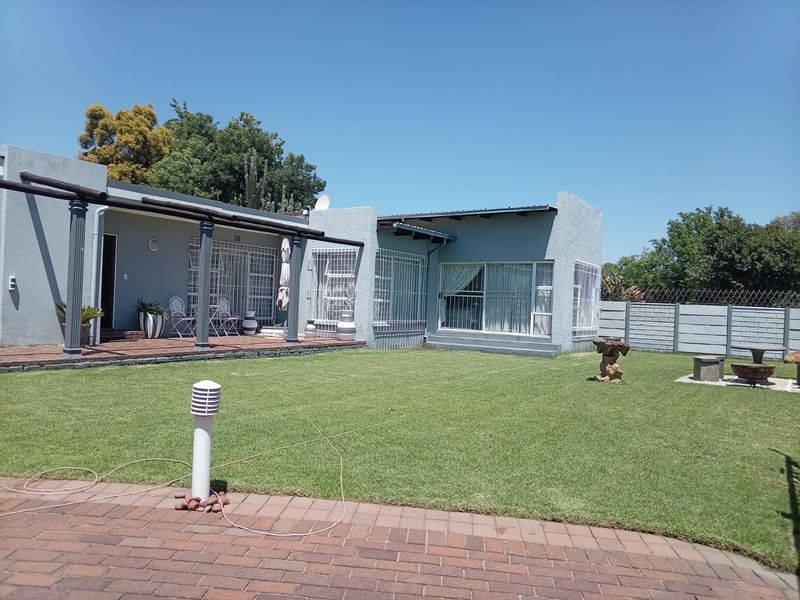 Rear view of the property featuring a covered patio, well-maintained lawn, and secure perimeter walling.