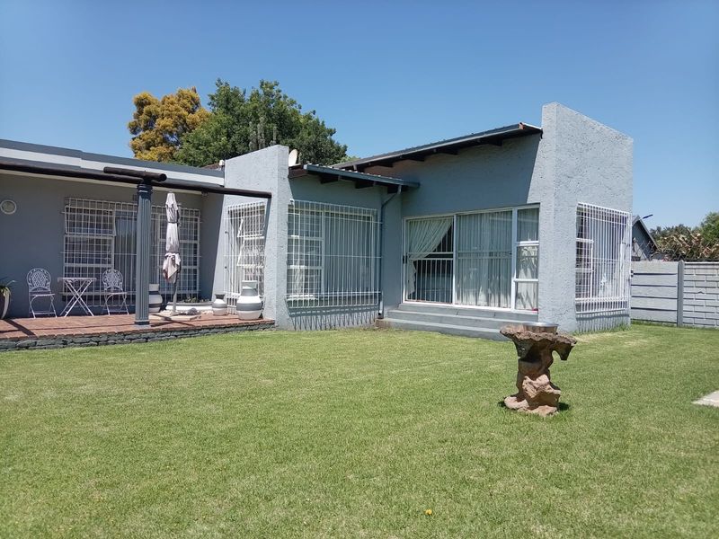 Rear view of the property featuring a tiled patio area, sliding glass doors with security bars, and a well-maintained lawn.