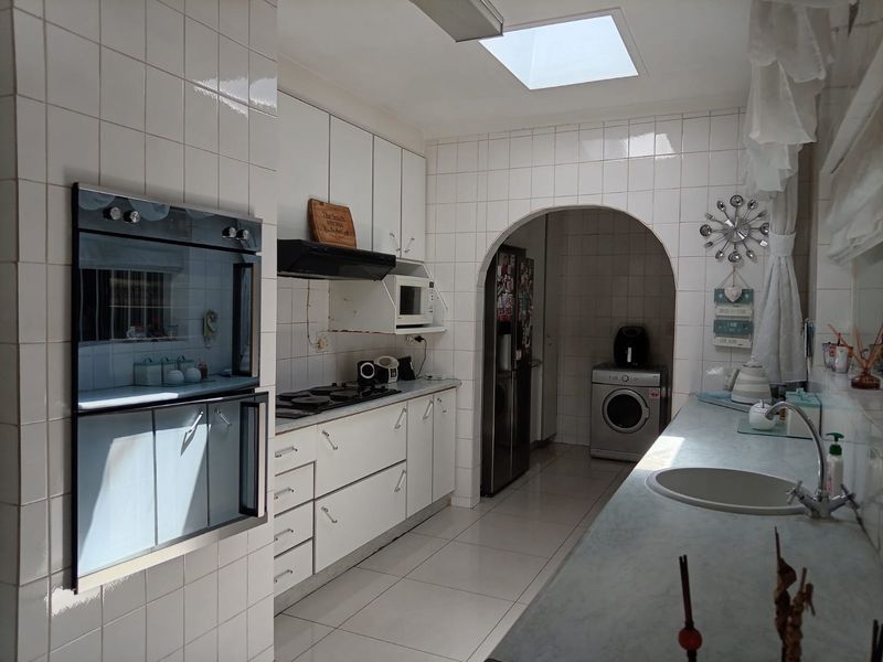 A functional kitchen featuring white cabinetry, built-in oven, hob, and a skylight, with an adjoining scullery area accessed through a classic archway.