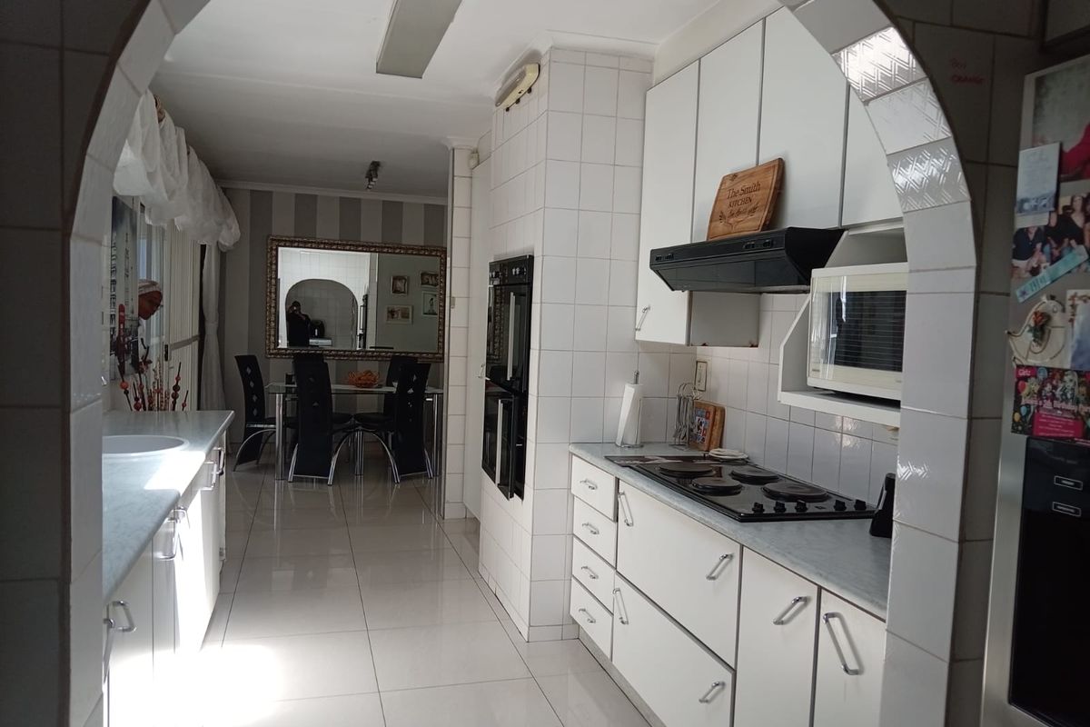 A functional kitchen featuring white cabinetry, tiled surfaces, and built-in appliances, framed by a classic architectural archway leading to the dining area.