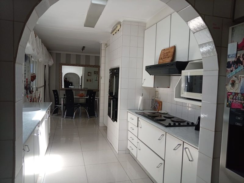 A functional kitchen featuring white cabinetry, tiled surfaces, and built-in appliances, framed by a classic architectural archway leading to the dining area.