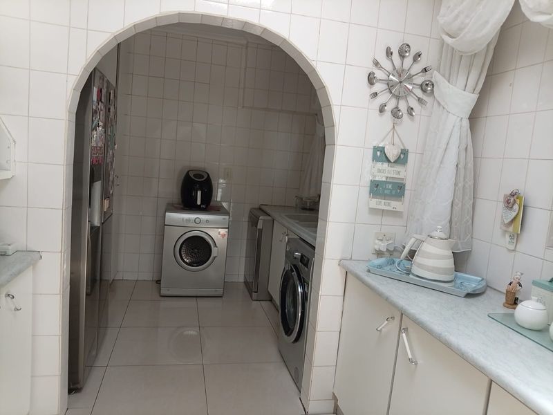 A functional scullery area featuring tiled walls and floors, built-in cabinetry, and laminate countertops, providing additional workspace and utility storage.