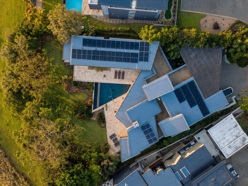 Aerial view of a modern residential property featuring a metal roof with integrated solar panels, a swimming pool, and landscaped garden areas.