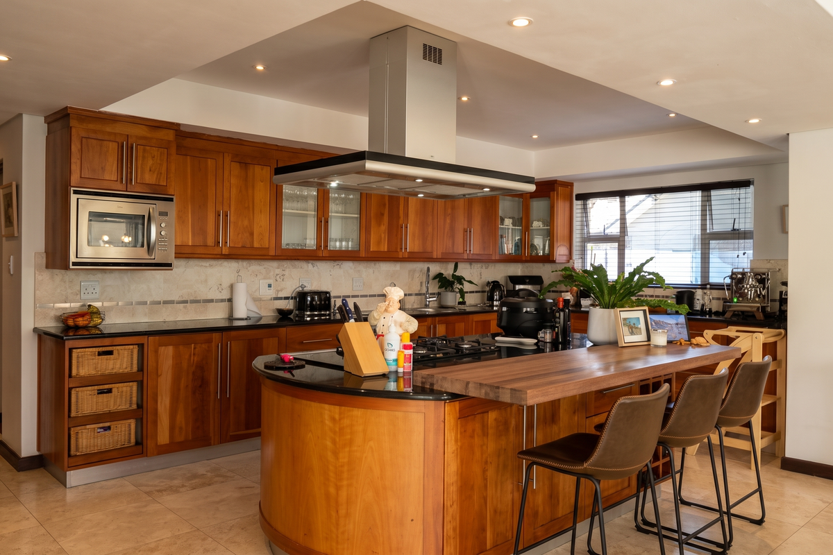 Spacious kitchen featuring warm wooden cabinetry, granite countertops, a large central island with breakfast bar, and integrated appliances including a gas hob and extractor.