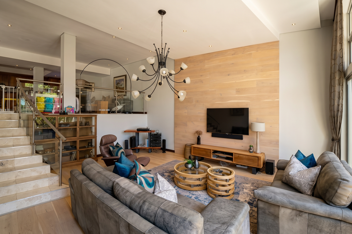 Spacious living room featuring timber wall cladding, stone staircase with glass balustrade, and large sliding doors opening to the garden.