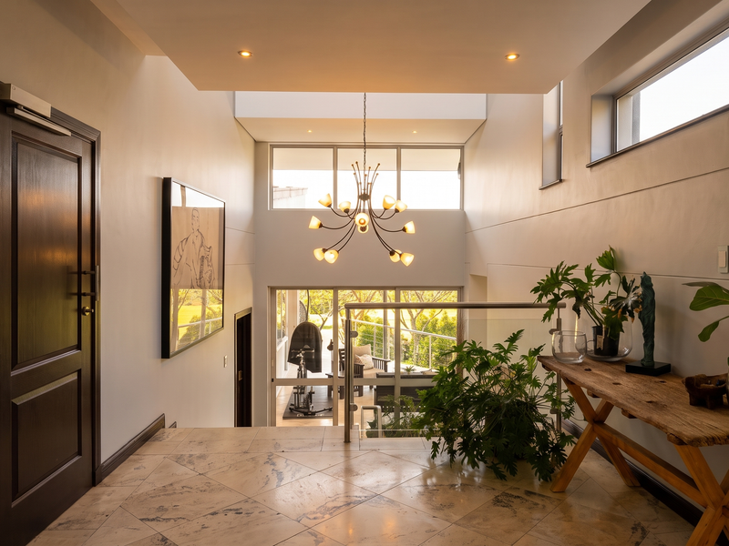 Spacious and bright entrance hall featuring high ceilings, elegant chandelier lighting, modern glass balustrade, and polished tiled flooring with views through to the rear.