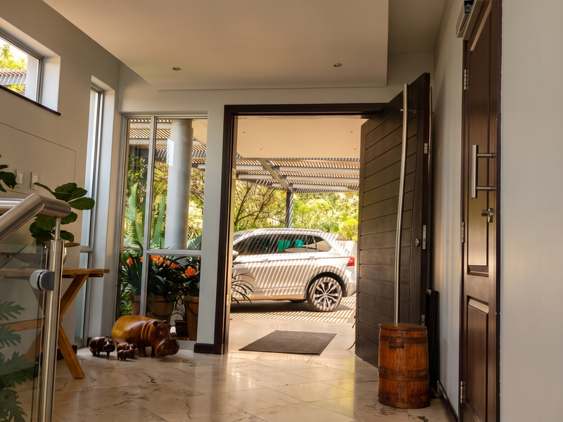 Modern entrance hall featuring polished marble flooring, a contemporary pivot door, and a glass-paneled staircase, providing a bright and welcoming transition into the home.