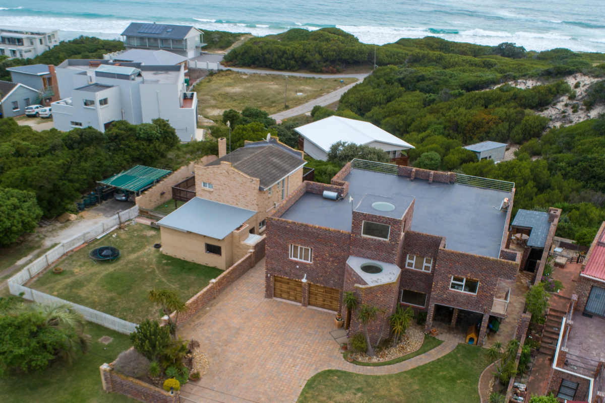 Aerial view of a multi-level brick house featuring a double garage, paved driveway, and flat roof, situated in a coastal neighborhood near the ocean.