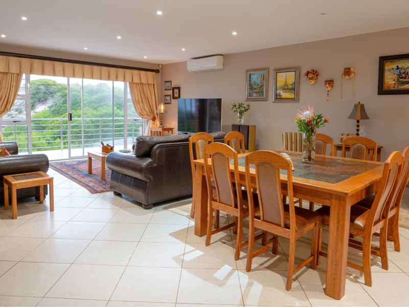 Spacious open-plan living and dining area featuring tiled floors, recessed lighting, and large sliding doors opening onto a balcony with scenic views.