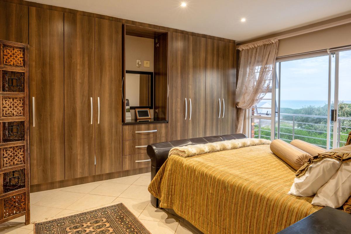 A well-maintained bedroom featuring extensive built-in wooden cabinetry, tiled flooring, and large sliding glass doors offering natural light and scenic coastal views.