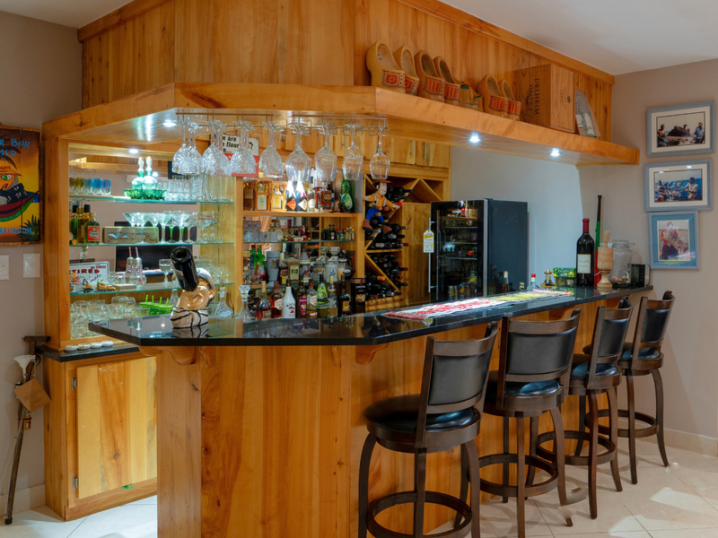 A custom-built wooden home bar featuring a granite countertop, integrated wine storage, glass shelving, and recessed lighting, creating a dedicated entertainment space.