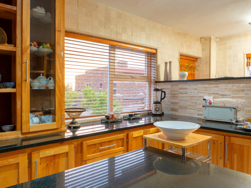 A well-maintained kitchen featuring warm wooden cabinetry, polished granite countertops, and neutral tiled backsplash with ample natural light from large windows.