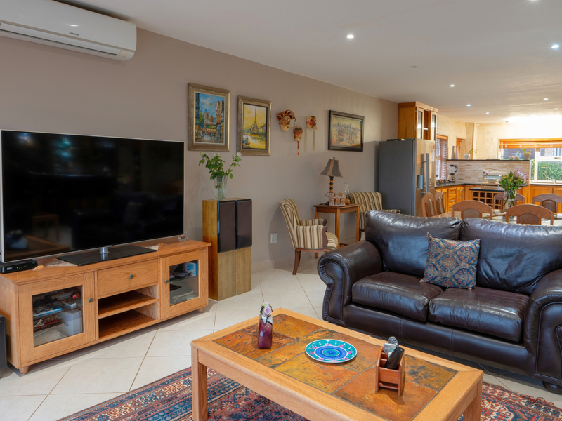 Spacious open-plan living and dining area featuring tiled floors, recessed lighting, a split-system air conditioner, and a stone feature wall leading into the kitchen.