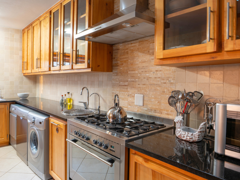 A functional kitchen featuring warm wooden cabinetry, granite countertops, a gas hob with extractor fan, and integrated laundry appliances.