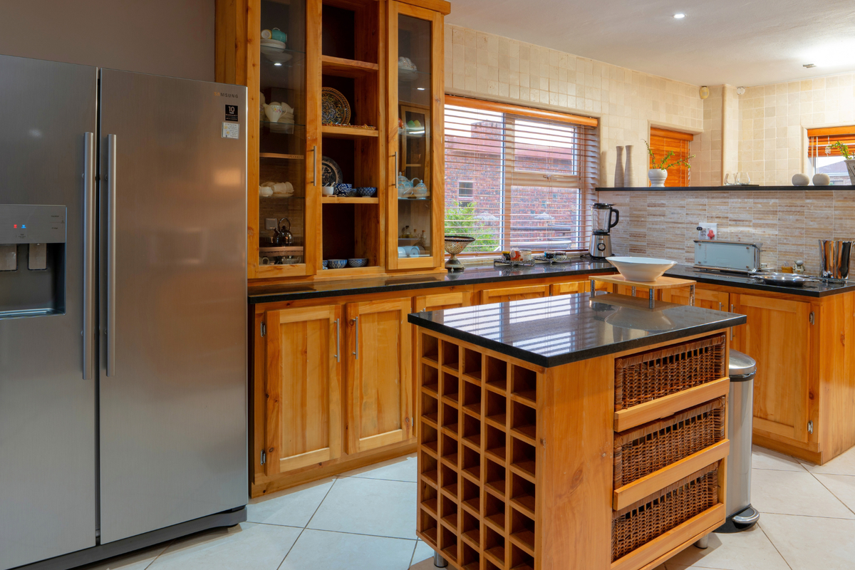 A functional kitchen featuring warm wooden cabinetry, granite countertops, a central island with integrated wine storage, and neutral tiled flooring.