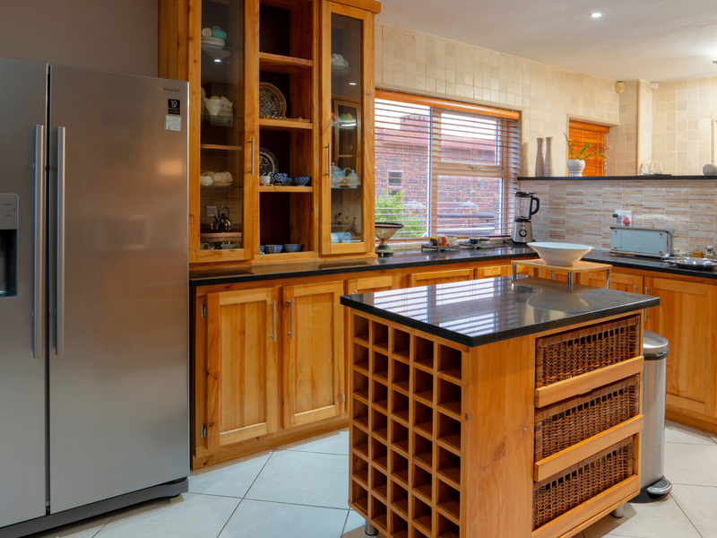 A functional kitchen featuring warm wooden cabinetry, granite countertops, a central island with integrated wine storage, and neutral tiled flooring.