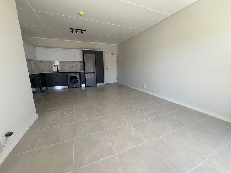 A modern, open-plan living and kitchen area featuring sleek cabinetry, marble-look splashbacks, and neutral tiled flooring in a clean, vacant space.