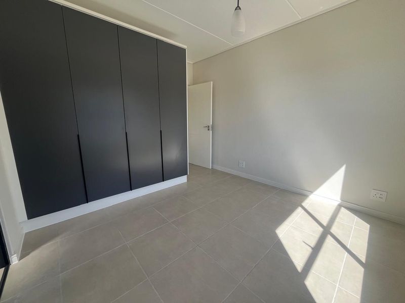 A bright, empty bedroom featuring modern dark built-in cupboards, neutral tiled flooring, and clean finishes, ready for personalization.